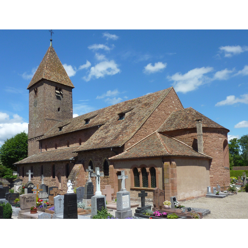 Source caption: "In der Mitte eines befestigten Friedhofs steht die romanische Kirche aus dem 11. und 12. Jahrhundert, einer der ältesten Sakralbauten des Elsass."