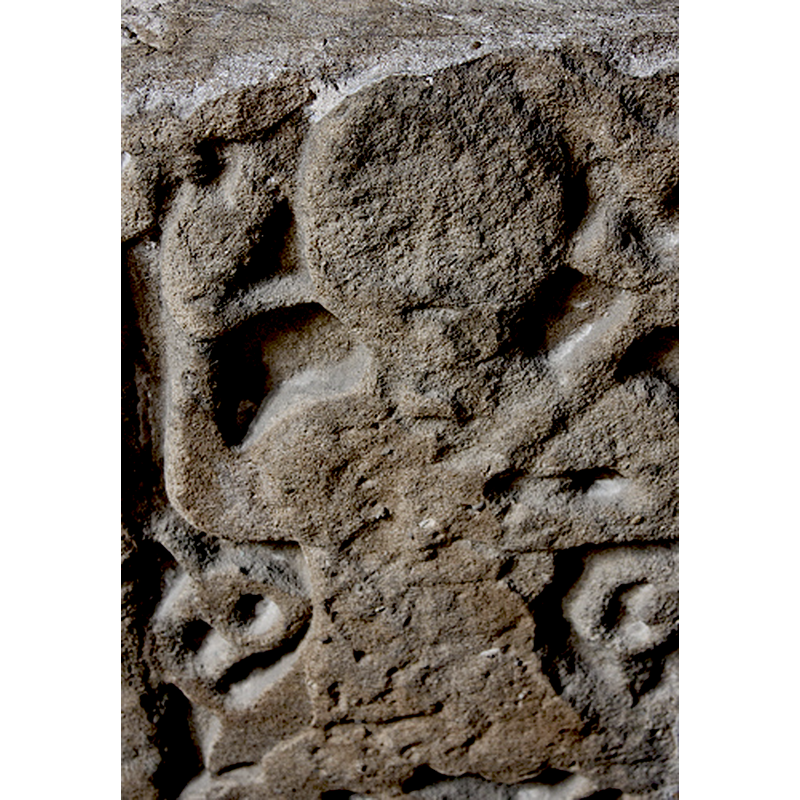 Source caption: "There are Saxon sculpture in the south aisle which may have belonged to a cross. There is a crude figure with a round head holding a cross and giving a blessing surrounded by scrollwork."