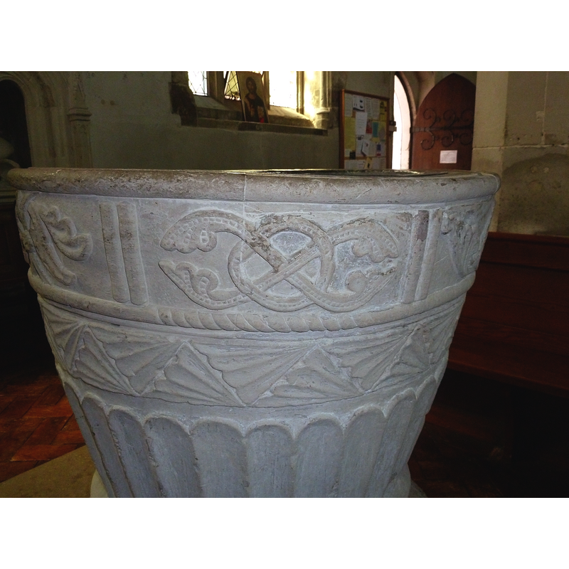 a band of individual foliage motifs, very ornate; the motifs are separated by vertical torsade or rope mouldings -- Source caption: "A side view of the wonderful C12th "Aylesbury" font in All Saints, Houghton Regis. The main pattern at the top here seems to have something of a Celtic influence. Note the somewhat wavy perimeter of the bowl."