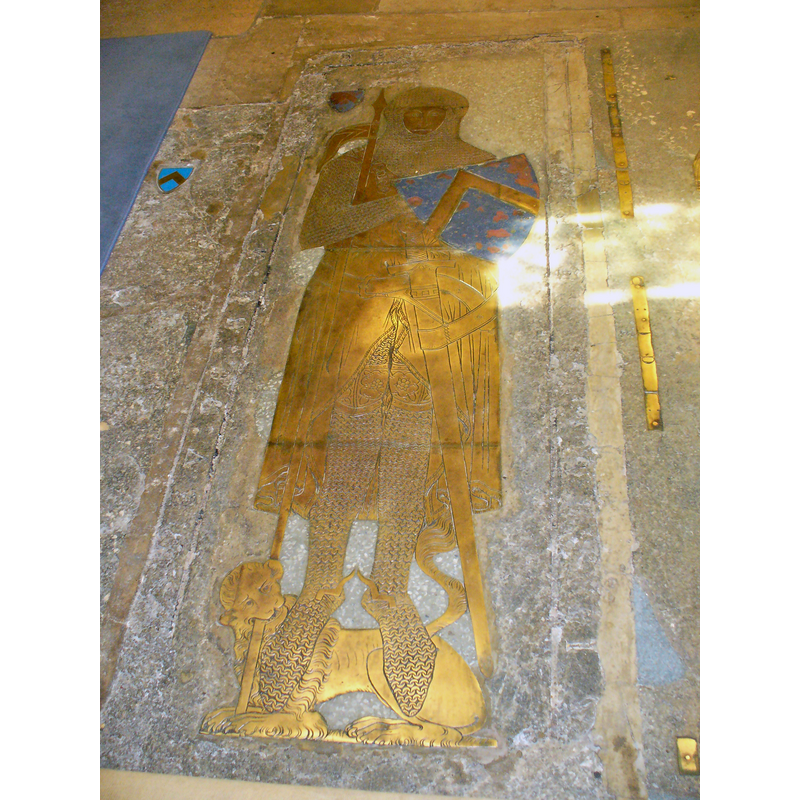13thC brass -- description quoted from the Victoria County History entry for this church (Surrey, vol. 2, 457-462): "In the chancel floor is a large slab, some 8 ft. long, of blue-grey marble. The margin is inscribed in sunk Lombardic capitals: 'Sire Johan Daubernovn chivaler gist icy Dev de sa Alme eyt mercy.' Let into the slab is a life-size brass of a knight in armour, the earliest now known in England; it dates from 1277. He is shown wearing a coif and camail of chain mail, the former strapped over the forehead. The hawberk reaches about two-thirds down the thigh, and the sleeves are corded at the wrists and terminate in mail mittens. The legs are encased in mail chausses fastened to kneecops of cuir bouilli which are ornamented with rosettes and an engrailed border. The mail is then continued as a thigh covering. There are no visible traces of a gambeson, though some such garment would certainly be worn. The surcoat is very ample and open in front from a little below the waist. The edge of this opening and the skirts, which reach to the bottom of the calf, are fringed. At the waist is a narrow plaited girdle. The sword is large, about 4 ft. long. The hilt has a large circular flat pommel, a corded grip, and short heavy quillons curving slightly downwards. The scabbard is tipped with metal and brought up into an obtuse V clasping the guard on either side. The sword-belt is broad and fairly plain, being merely ornamented with a stitched border and punched work at the buckle-holes. The frog is elaborately arranged to cant the sword at a slight angle, and the whole belt passes diagonally round the hips. The shield is small and heater-shaped and bears: azure a cheveron or, the field being enamelled. The cheveron is drawn very narrow and is carried up to the top of the shield. The shield, resting on the left arm, is slung over the right shoulder by a broad belt ornamented with a rose and swastica and having a broad buckle. In the crook of the right arm is a lance some 6 ft. long, without grip or vamplate, and with a small fringed pennon bearing a cheveron. Plain prick spurs are worn with a rather thin strap. The hands are joined in prayer, and the feet rest upon a lion which bites the butt of the lance."
