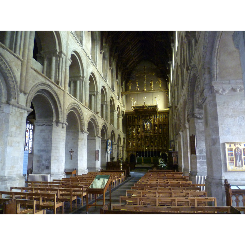Source caption: "The Norman nave of Wymondham Abbey. Wymondham Abbey was founded in 1107 by William d'Albini, Chief Butler to Henry I as a cell for his brother's abbey in St Albans. When it was built it was intended to serve both the Benedictine monks and the parishioners of Wymondham, but the rights of each were unclear from the start and this led to many quarrels between the two. These often concerned the hanging and ringing of the parish bells. After the Priory gained its independence as an Abbey from St Albans in 1448 and the great west tower was provided by local people, these problems largely disappeared. 
At the Dissolution of the Monasteries in 1538, the Abbey church was granted to the people of Wymondham for a payment. The east end of the church, which was where the monks had worshipped, was gradually dismantled and the materials sold off. The nave was blocked off at the former crossing tower and the ruined Monks' Tower was left standing. The nave seen here still has its original round Norman arches built of stone from Caen in Normandy. During the 1400s the roof was raised and the north aisle rebuilt and enlarged. It was at this time that the bell towers were re-built, with the one at the east for the monks and the one at the west for the parishioners. The screen at the end was designed by Sir Ninian Comper to partly cover the bare wall where the entrance to the monks' church."