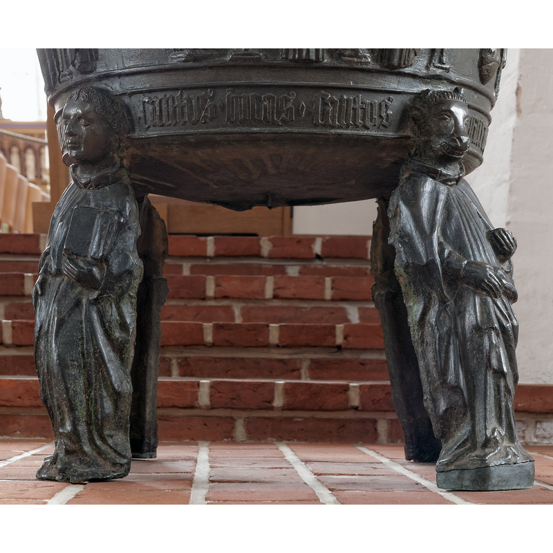 not the usual representation of Matthew, the Evangelist; seen here on the left, it consists of a human figure holding an open book in the left hand; since the other three standing figures have as heads those of their synbols, this one must therefore be an angel's head -- the inscription on the lower end of the basin, between the heads, identifies Luke, the Apostle on the right