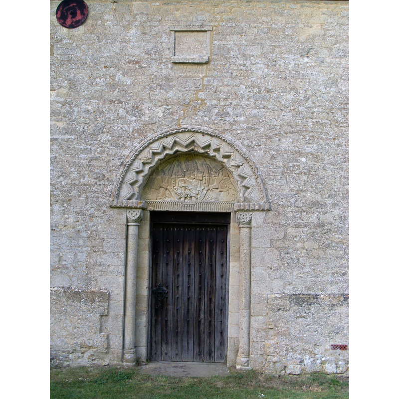 Source caption: "South Door, St Giles Parish Church. This photo shows the south (main) entrance to the Church. Above the door can be seen a 12th Century Norman tympanum carved with a Christ in Majesty seated on a throne and supported by two well-feathered angels in flowing drapery. The lintel has a pattern of delicate intersecting arches."