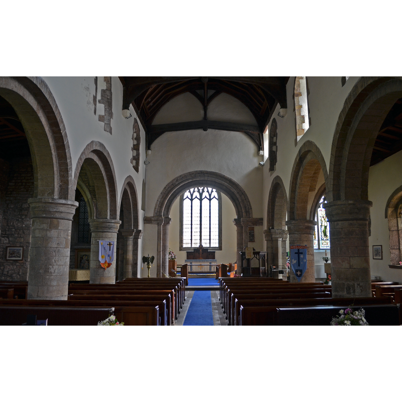 Source caption: "The nave has 12th century clerestory windows with a corbel table. The arcades are of four bays, with round arches and circular piers. The north aisle has the remnants of a stone seat which was used by the old, weak and sick. The chancel arch is 12th century and is richly moulded. There is a rood doorway to the left."