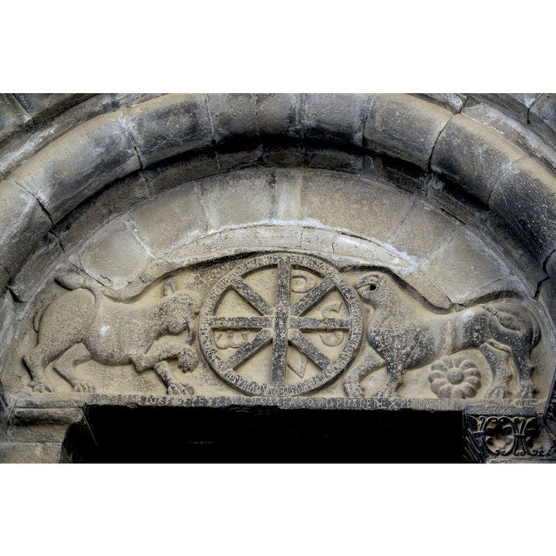 Source caption: "Portal der Westfassade, Tympanon, Darstellung: zwei Löwen und Chrismon; lateinische Inschriften auf dem Rand des Kreises (Übersetzung: „Ich bin die einfache Tür, tretet ein durch mich, Gläubige, ich bin die Quelle des Lebens, habt mehr Durst nach mir als nach Wein, alle, die ihr in diesen seligen Tempel der Jungfrau tretet.“) und auf dem Türsturz (Übersetzung: „Bessere dich bevor du Christus anrufst.“) (s. Erklärungstext in der Kirche)" -- Transcription of the Latin inscription by A. Garcia-Omedes [www.romanicoaragones.com/0-Jacetania/23-SerosStaMaria2.htm] [accessed 29 June 2016]: on the circle of the chrismon "+IANVA SVM P-PES-P PER ME TRANSITE FIDELES FONS EGO SVM VITE PLUS ME QVAN VINA SITITE VIRGINIS HOC TEMPLUM QVIS(QVIS) PENETRARE BEATUM"; below: "CORRIGE TE PRIMUM VALEAS QUO POSCERE CHRISTUM"