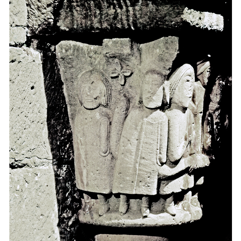 eastmost capital on the north side of the cloister; this side shows two fully dressed figures wearing shoes and standing full frontal; between them is a serpent; above the serpent's head (?) is a four-petal flower; the body of the serpent continues towards the right onto the adjacent face of the capital