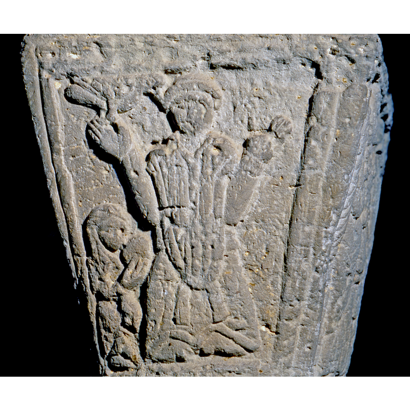 this capital appears different in style and composition from the majority of the others in this cloister; this side shows a tonsured priest in orante pose with a smaller figure kneeling (?) besides him; a bird by (on?) the priest's right hand, the beak near his ear