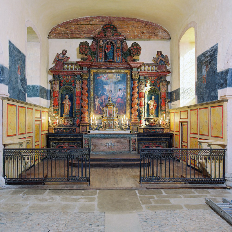 Source caption: "Le retable du maître-autel a été commandé à Pierre Duhamel en 1686. Sa restauration a mis en valeur la richesse de sa polychromie et révélé la peinture sur bois qui en occupe le centre, la Lapidation de saint Etienne, œuvre d’un peintre local. La statue de saint Marcel occupe la niche du couronnement, celles des ailes abritant les représentations de saint Pierre et saint Paul, dans un foisonnement d’anges et d’enroulements en forme de panache."