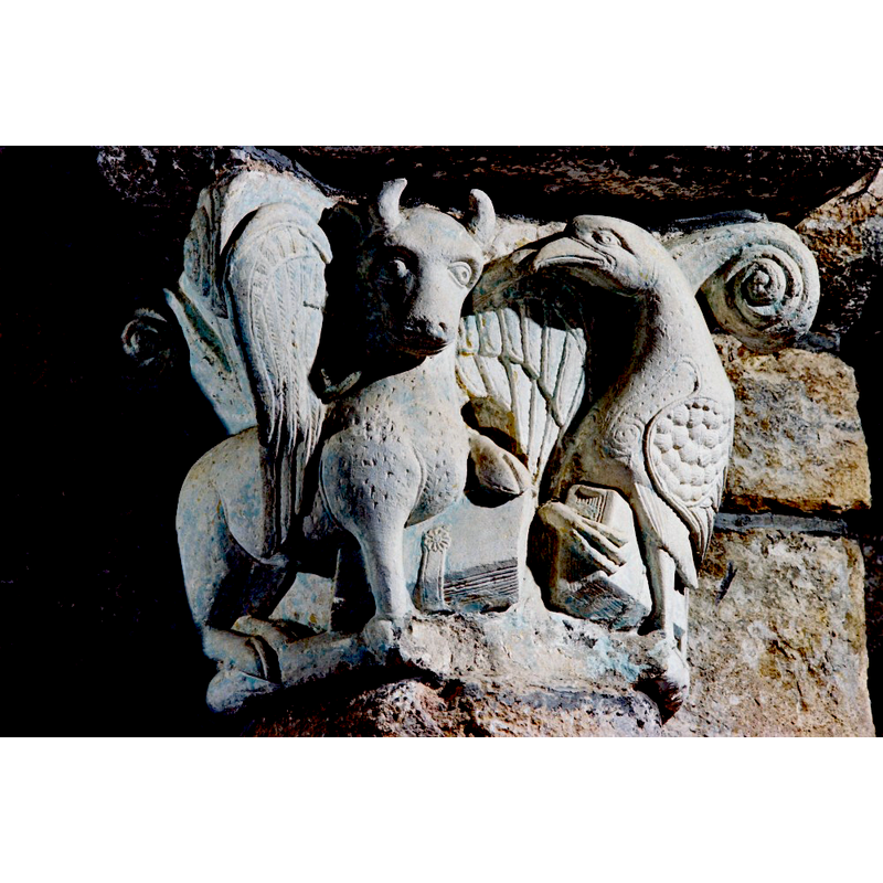 Source caption: "L’arc triomphal qui s’ouvrait sur le chœur disparu, est orné de deux chapiteaux remarquables où figurent, groupés deux par deux, les symboles des évangélistes : le taureau de saint Luc et l’aigle de saint Jean au sud, le lion de saint Marc et l’ange de saint Matthieu au nord."