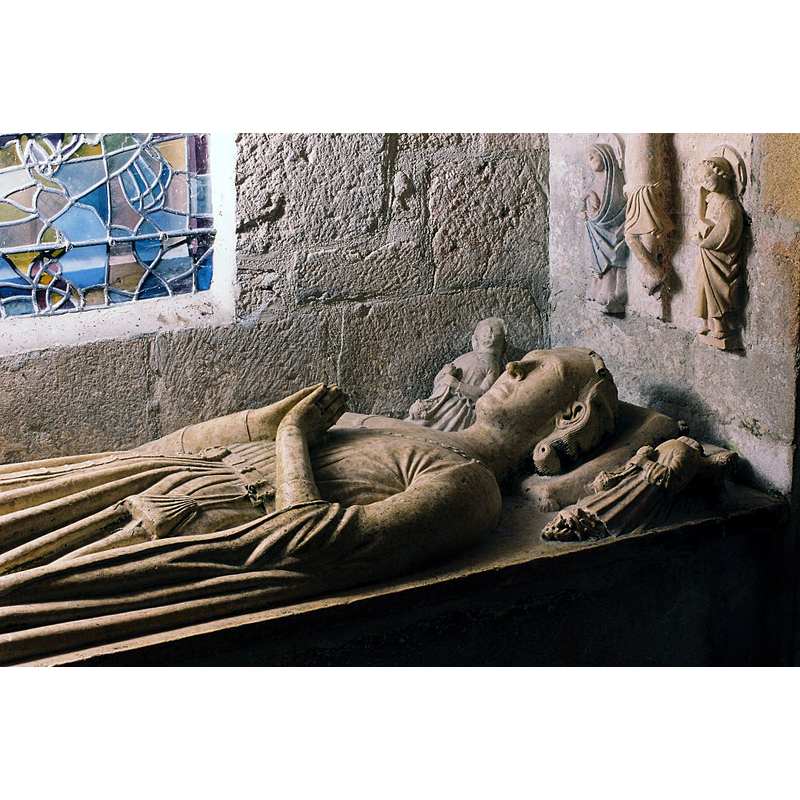 Source caption: "Dans la chapelle sud, éclairée par des vitraux de Léon Zack (1971), un enfeu du XIVe siècle abrite une statue de chevalierveillé par des anges. Le dragon et les deux charmants moines lisant de chaque côté du gisant proviennent peut-être d ‘un autre ensemble. A la tête du défunt,figure le Christ en croix entre la Vierge et saint Jean; à ses pieds, saint Martin partageant son manteau avec un pauvre et un donateur."