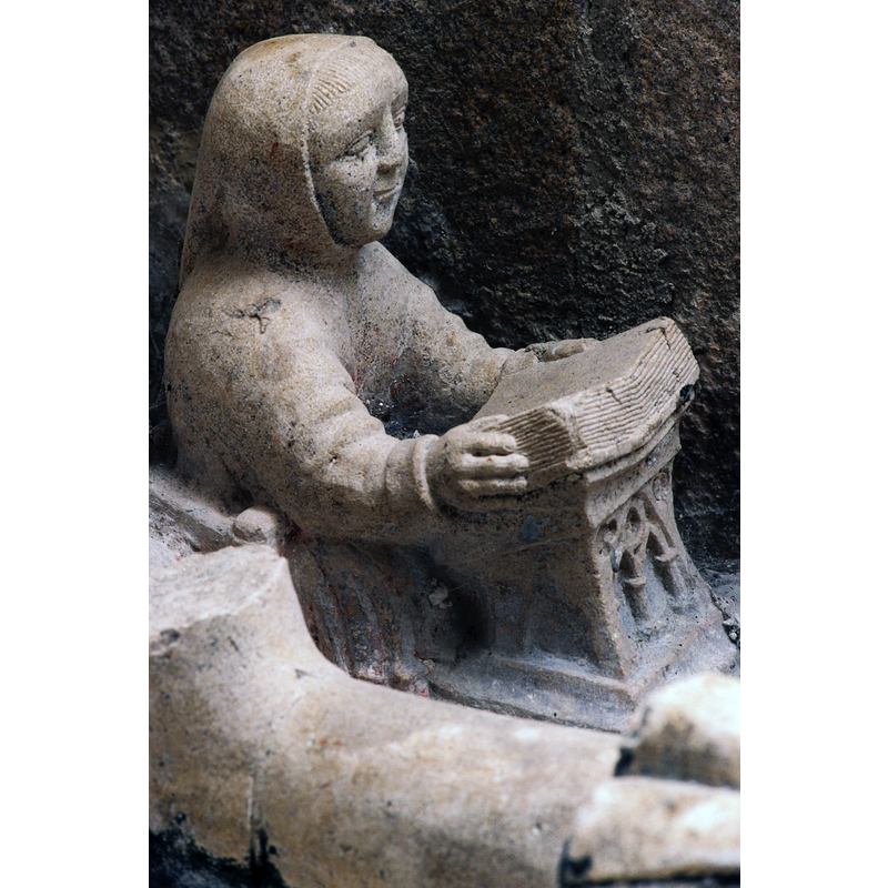 Source caption: "Dans la chapelle sud, éclairée par des vitraux de Léon Zack (1971), un enfeu du XIVe siècle abrite une statue de chevalierveillé par des anges. Le dragon et les deux charmants moines lisant de chaque côté du gisant proviennent peut-être d ‘un autre ensemble. A la tête du défunt,figure le Christ en croix entre la Vierge et saint Jean; à ses pieds, saint Martin partageant son manteau avec un pauvre et un donateur."