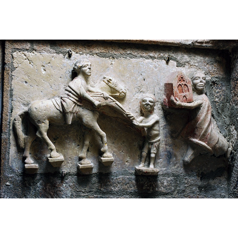 Source caption: "Dans la chapelle sud, éclairée par des vitraux de Léon Zack (1971), un enfeu du XIVe siècle abrite une statue de chevalierveillé par des anges. Le dragon et les deux charmants moines lisant de chaque côté du gisant proviennent peut-être d ‘un autre ensemble. A la tête du défunt,figure le Christ en croix entre la Vierge et saint Jean; à ses pieds, saint Martin partageant son manteau avec un pauvre et un donateur."