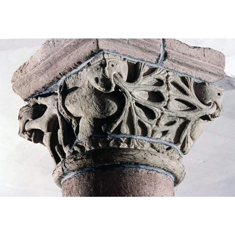 Source caption: "A l'intérieur, un chapiteau présente un décor végétal." It has a lion at each angle with palmette-shaped vegetation stemming from the mouths.