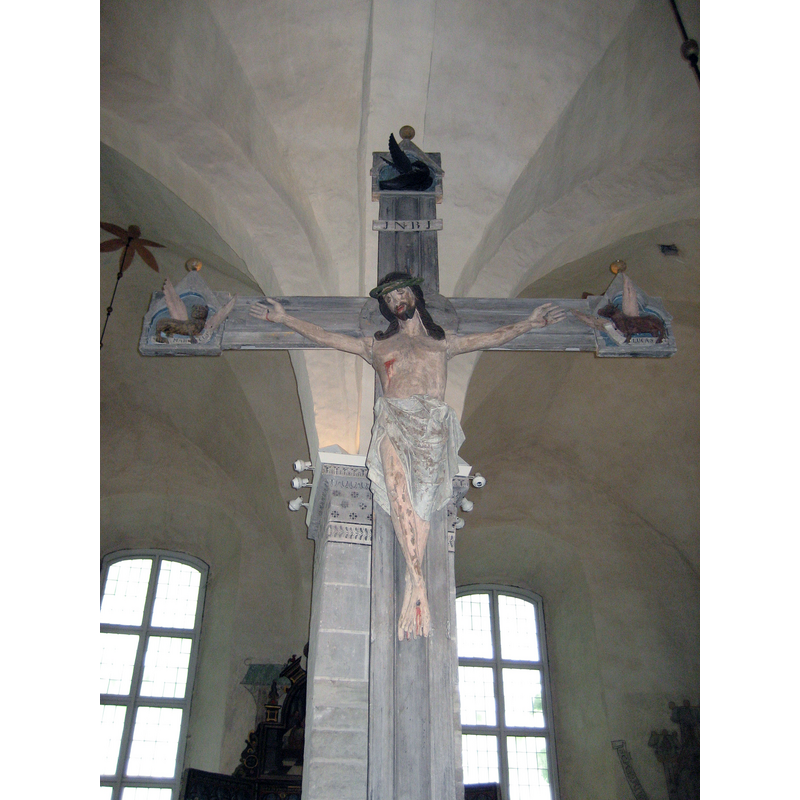 "The Triumphal crucifix from Sund, originally a ring crucifix of Gotland type, has been dendrochronologically dated to the 1250s. The oak of the body of Christ was felled in the Schleswig-Holstein area in the 1240s. And the same goes for the apostles in the aediculas at the end of the cross arms. The rest of the wood has local origin: The giant cross (5,06 m high) itself is of elder, cut in the elder wood which still grows along the shores of the nearby lake, while the plugs that join the arms of Christ to his body, is of pine. Also the ring itself was of pine. Thus we have an early example of collaboration between foreign import and local workshops. The crucifix must have been ultimately assembled in Åland, which also means that the final coat painting of the crucifix was done locally.  The crucifix was mounted on a ”trabes” a cross beam between the chancel and the congregation part of the church, where it formed a part of the Calvary group, flanked by Mary and John in Mourning. Today Mourning John is missing." [source: Åsa Ringbom 2012  [www.kyrkor.ax/churches/sund-church/] [accessed 26 July 2017]]
