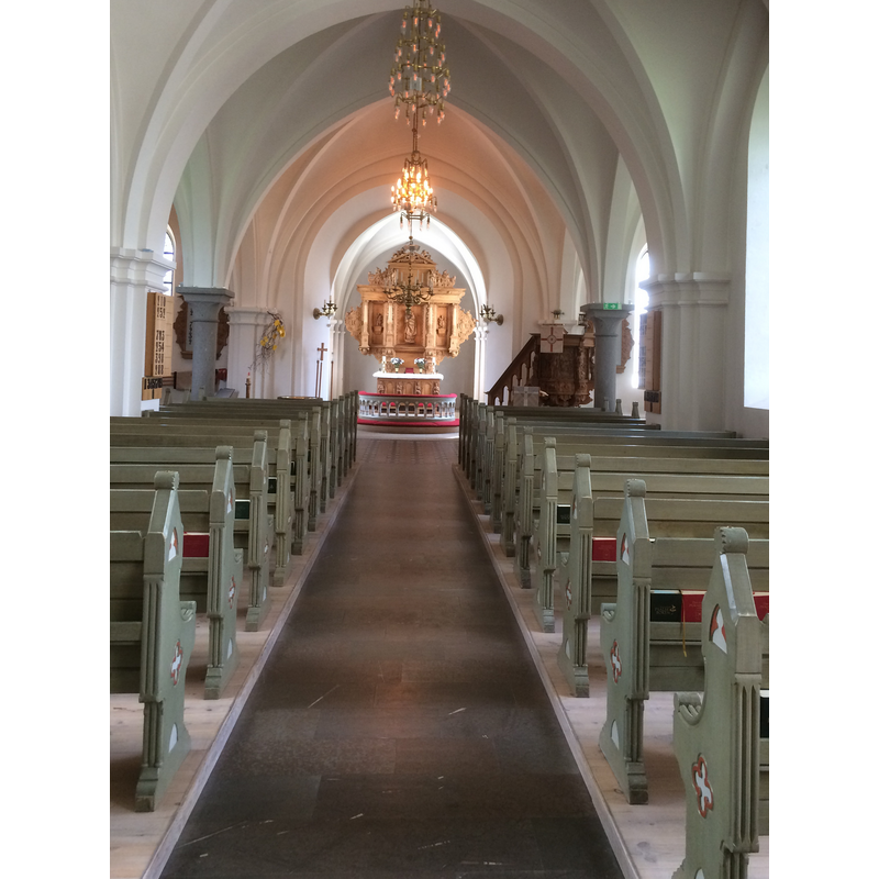 the top of the font and its baptismal dish are barely discernible at the far end of the left bank of benches