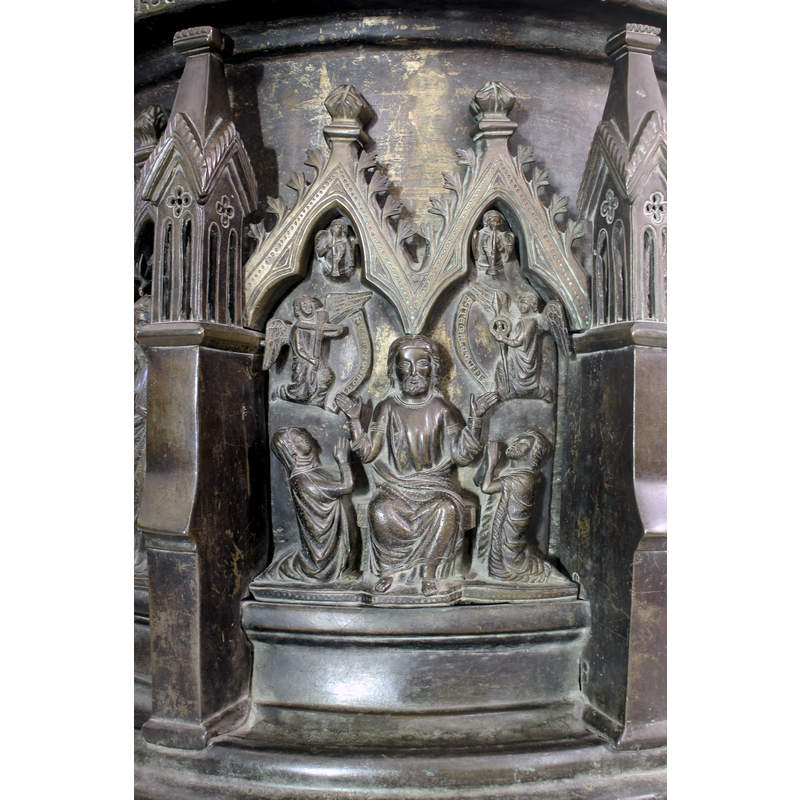 the composition includes two small angels playing trumpets in the trefoiled arch-heads atop; two larges angels hold objects (the one on the left holds a cross; the one on the right a wreath or crown of thorns and a spear); inscribed scrolls on the sides; Christ sits with arms in orant position; no halo; to the sides of Christ kneel a woman (left) and a man (right) [patrons?]