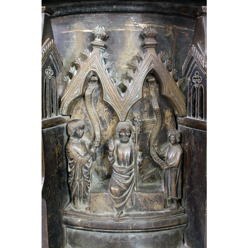 Christ steps out of the grave, his right hand raised in benediction, his left hand carries a processional cross with a banner that bears a further cross; two fugures stand on the sides holding inscribed sctolls; the one one the left has a tonsured head and wears rich clerical garb that is inscribed on the right shoulder; the one on the right, probably an accolite, wears a simple tunic; there are no figures of the soldiers present, but they and their weapons are incised on the front side of the grave
