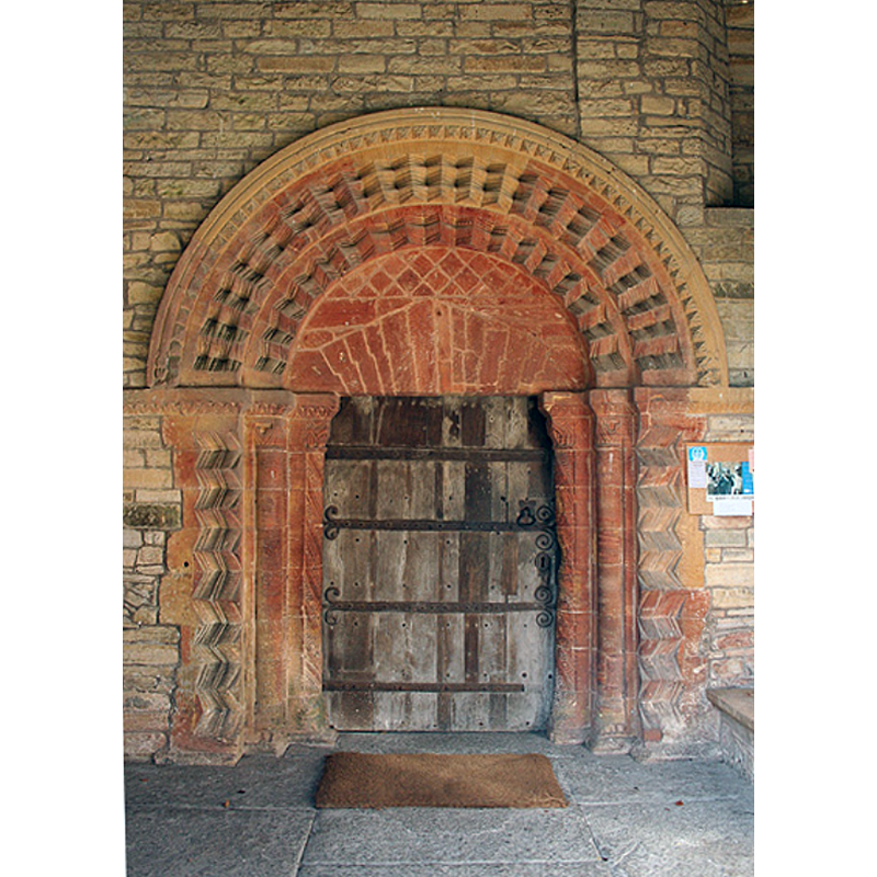 Source caption: "Huish Episcopi: south door, St Mary’s church. A splendid 12th century Norman doorway, said to be reddened by fire damage in the 13th century. The fire destroyed much of the early church and the present structure is largely Perpendicular Gothic."