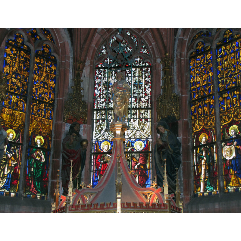 the finial of the font cover against the neo-Gothic background of the Chapelle de la Trinité -- the finial may be John the Baptist or, given the garments, Peter