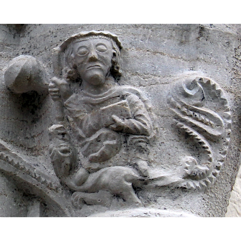 detail on the eastmost capital of the east side of the portal -- the human figure holds a weapon in his right hand with which he stabs the long-tailed dragon through its open mouth; he holds a closed book in his right hand ; the dragon's tail is most elaborate