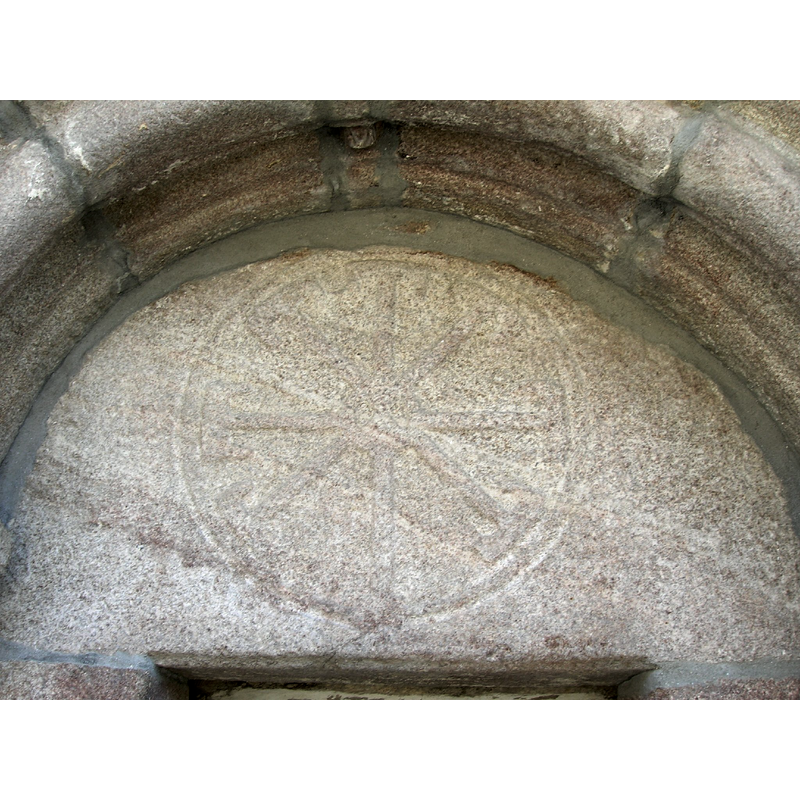 Source caption: "El tímpano está decorado con una cruz de 8 brazos acabados en forma de T, inscrita en un circulo."