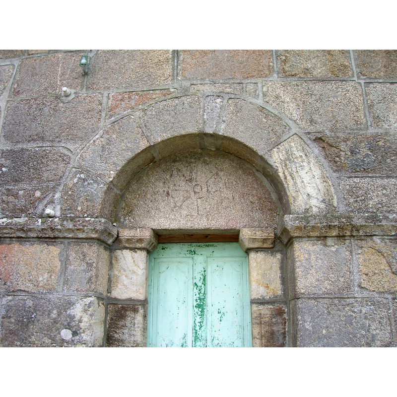 Source caption: "Portada norte con arco de medio punto formado por dovelas y tímpano con el relieve de una cruz de 8 brazos inscrita en un circulo."