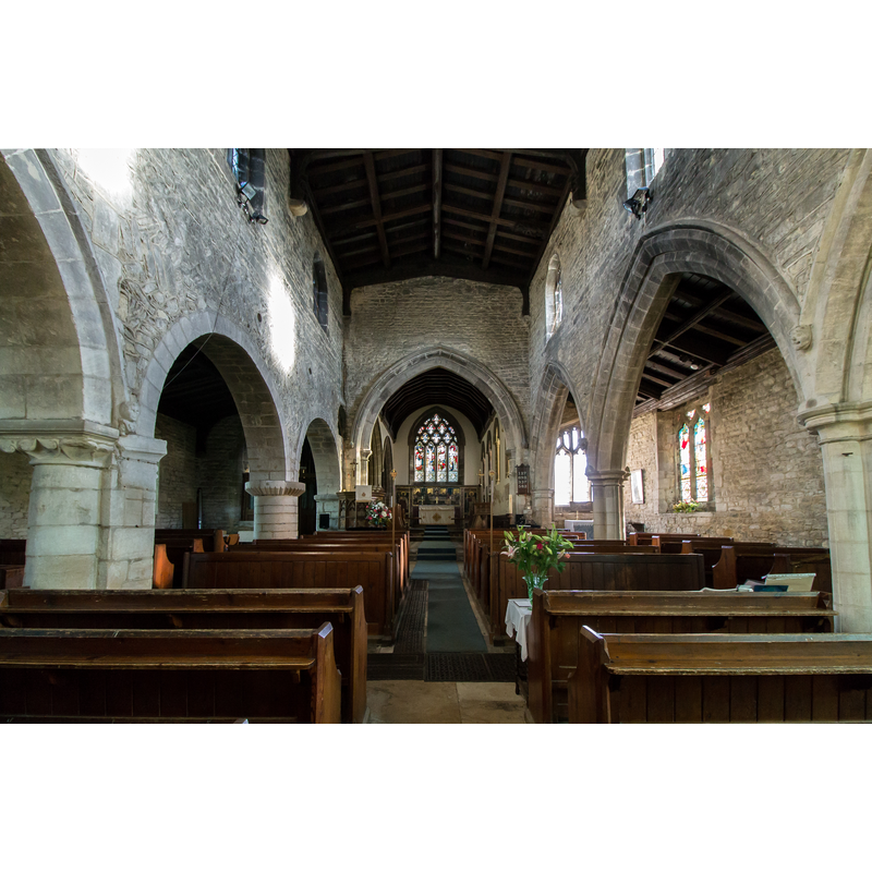 Source caption: "Interior, St John the Baptist church, Colsterworth [...] The original church consisting of nave and chancel, was built in herringbone coursing with small round-headed windows, was here in the year 1000. The last of the herringbone walling can be seen above the North Arcade and in the corner of the Lady Chapel above the South Arcade. The church consists of western tower, nave, clerestory, aisles, south porch, chancel, north organ chamber and vestry. The tower is of 3 stages and made of ashlar. The mason was Thomas de Somersby as inscribed on the southern base plinth of the tower. With such a massive structure, the walls are four feet thick; it almost certainly had a spire as depicted in a sketch by the young Isaac Newton on the kitchen wall of the Woolsthorpe Manor, drawn around 1650. The four gargoyles, water outlets no longer in use, tend to support this assumption. Behind the organ is a sundial carved by the young Isaac Newton with his pen knife at the age of 9 at Woolsthorpe Manor. It was built into the wall at the time of the chapel's reconstruction and a bust of Newton was carved into the corbel above it. This work was carried out by the Turnor family and the sundial given by C. Turnor Esq. The octagonal font has part C15 stem with panels in part bearing pointed arches containing sacred symbols and floriate designs, and also C12 billet moulded blank arcading, the panels filled with fleurons and trefoils. The C19 bowl repeats this theme. In 1876 the chancel was rebuilt by James Fowler of Louth."