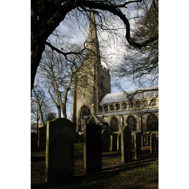 Source caption: "Gravestones in shadow in All Saints' parish churchyard, Holbeach, Lincolnshire, with the west tower and spire in the background".
