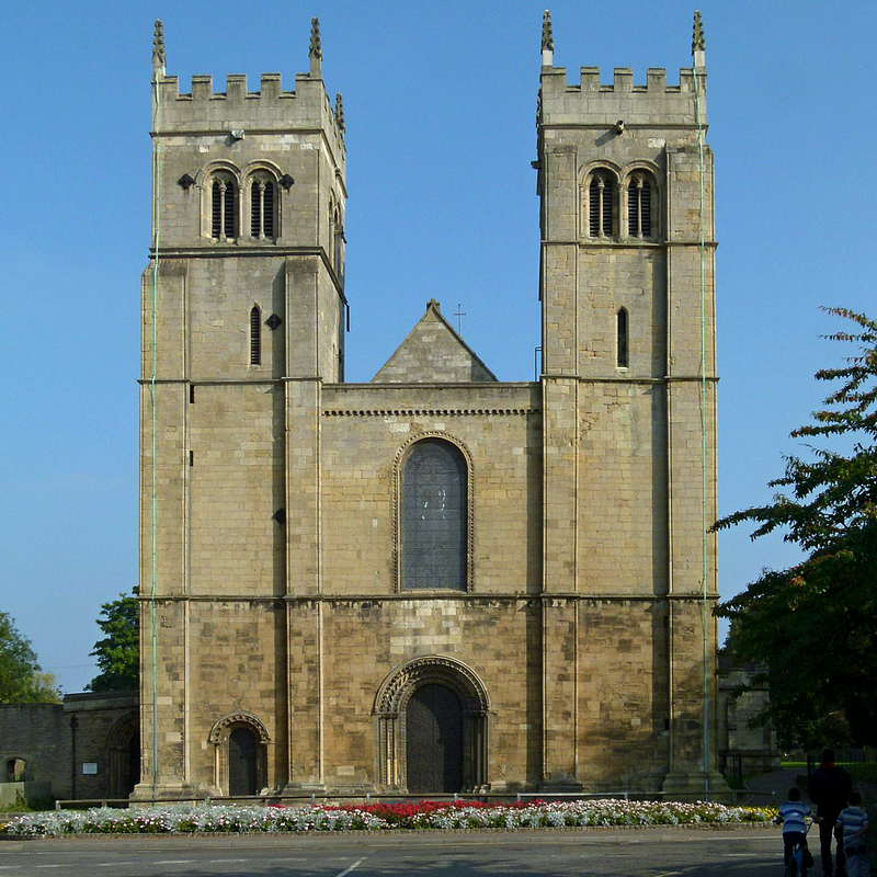 Source caption: "Worksop Priory, west front. [...] The front remains – unusually – virtually as built in the 12th century, the most obvious addition being the later (14th century) crenellation."
