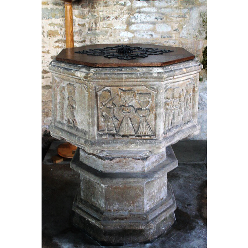 Source caption: "Just inside the church is the font – the base and stem are Early English but the octagonal bowl is believed to be 16th century, judging by the costumes of the figures, but carved in an archaic crude style with biblical and symbolic figures,the underside of the bowl is also decorated with carved figures."