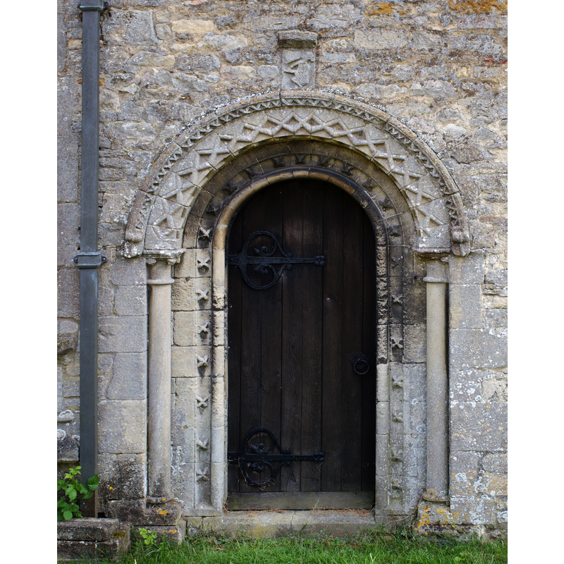 Source caption: "The North, or "Devil's" door has a typical Norman arch of about the 12th Century. It is surmounted by a curious carving of a dancing figure, perhaps meant to be Old Nick himself?"