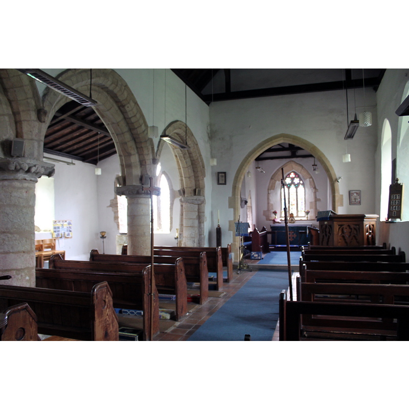 Source caption: "The late 12th century north arcade is of three bays, with square bases which may be older. The circular piers have leafed capitals and human head label stops. There are traces of paint on the arcade with black and yellow chevrons on the inner order of the eastern arch.[...] The chancel arch is 19th-century".
