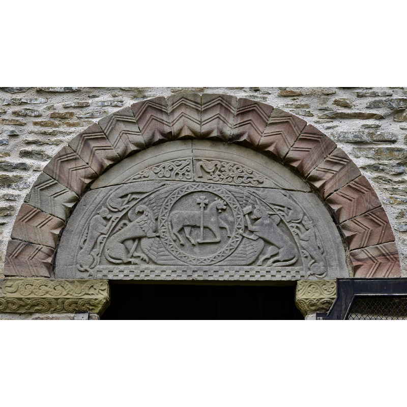 Source caption: "Pipe Aston: St. Giles' Church: The tympanum [north portal]. In amazingly good condition considering its age, the carving of the "agnus dei" flanked by a winged eagle and a winged bull is still sharp and defined." -- "Mr. Romilly Allen pointed out that the confusion or association of the grifñn with the symbols of the four Evangelists was to be found in Byzantine art, as in the mosaic decoration of the marble parapet in the church of St. Lucia (Gaeta circa A.D. 1000), and that another instance occurred on the font in Lincoln Cathedral." [cf. FontNotes]