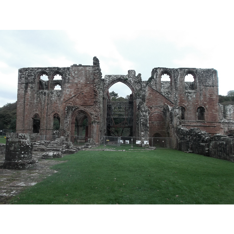 Source caption: "Furness Abbey - Nave and Transepts. Little remains of the nave of the great abbey church at Furness, the grassed area seen here being the floor with the stumps of pillars to the left and low wall to the right being the only remaining masonry. Ahead however are the much more substantial remains of the Transepts with the North to the left and South to the right of the central arch marking the Crossing, with the Presbytery and eastern end of the church (originally containing the High altar) leading on from this."