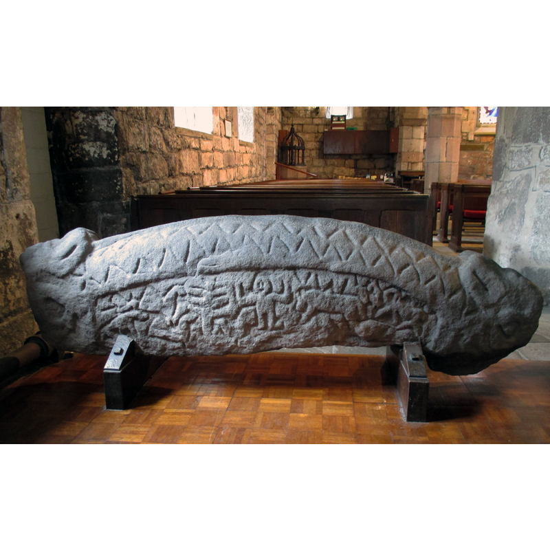 Source caption: "Hogback tombstone in St Peter's Church, Heysham, Lancashire." An additional caption from a photograph of this tombstone by Humphrey Bolton [https://commons.wikimedia.org/wiki/File:Hogsback_tombstone,_St_Peter's_Church,_Heysham_(2)_-_geograph.org.uk_-_439403.jpg] [accessed 3 April 2019] reads: "Hogback tombstone, St Peter's Church, Heysham (2) This side of the stone tells the story of Sigurd the dragon-slayer. Rather than the horse and lance of St George, Sigurd dug a pit and thrust his sword up into the unprotected belly of the dragon Fafnir from below. He had been advised to dig an escape tunnel and a trench down from the pit so as not to be trapped and drowned in the dragon's blood. This dragon was like a serpent, without legs. Signund's horse Grani is also depicted, and also the tree Yggdrasil, with birds."
