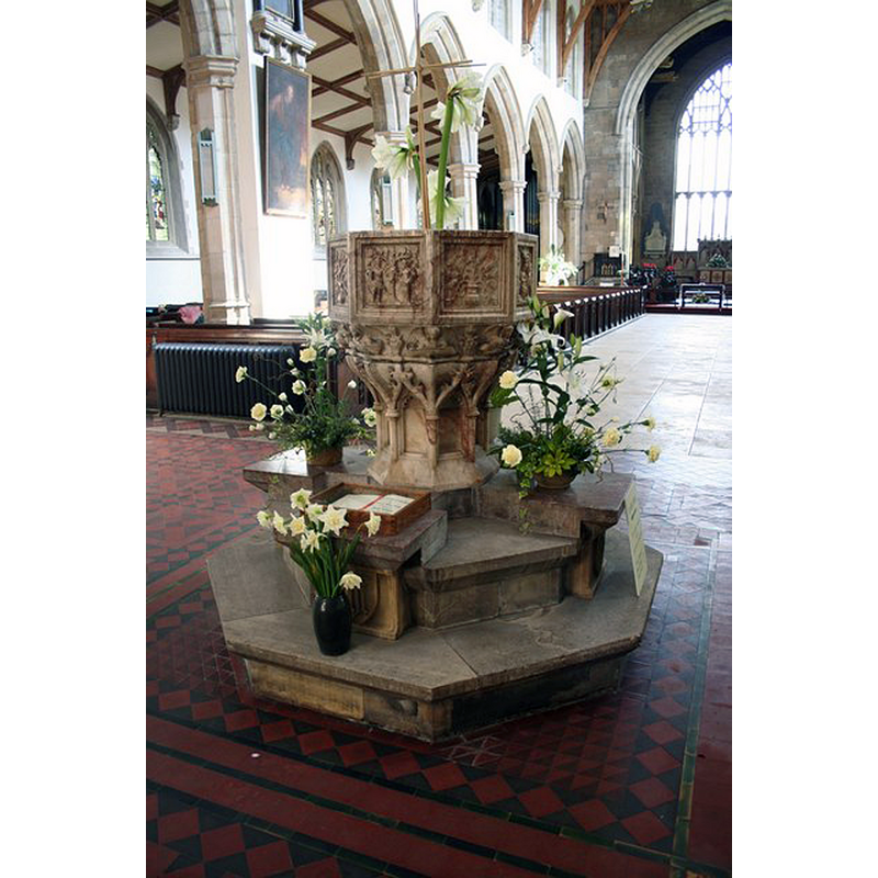Source caption: "St.James' font. Staffordshire alabaster font from James Fowler's restoration of 1868-9 replacing the 15th century font LinkExternal link Its panels shows scenes of Christ's baptism, crucifixion, Adam & Eve and Noah's Ark".