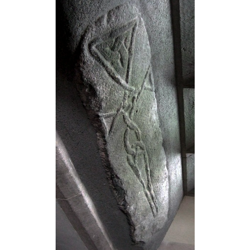 Source caption: "The Cross Stone at Nevern church. The image has been deliberately rotated to show the carving in an upright position.. The (unascribed) booklet obtainable within the church describes the complex interlacing of the cords running along the limbs of the cross as unusual and suggestive of an advanced date. Dillwyn Miles in A Book on Nevern quotes Dr Nash-Williams as stating that the pattern is typically Irish in form and dates from the C10. (To my eye the motif has a decidedly humanoid shape.)"