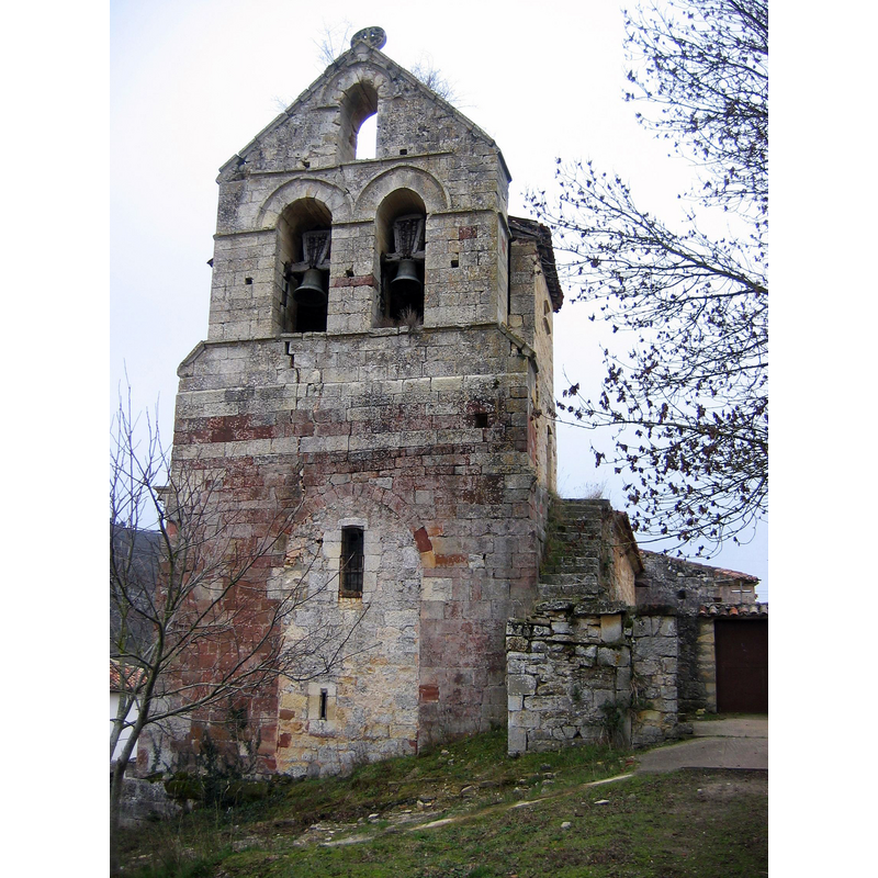 Source caption: "Iglesia de San Pedro en el Barrio de San Pedro, Becerril del Carpio (Palencia, Castilla y León). En altura destaca una espadaña sobre el hastial, en la que una inscripción visible bajo las ventanas leemos "ERA MCCC FIZO" (1262), ilustrativo ejemplo de la persistencia de formas románicas hasta bien entrada la mitad del siglo XIII. Esta espadaña tiene tres niveles: el inferior cobija la primitiva portada que daba paso a la iglesia desde el hastial,- el segundo nivel tiene dos troneras de chambrana e imposta nacelada y el tercero, con remate a piñón, está perforado por una única tronera con chambrana y reducida imposta. Se remata con una magnífica cruz flordelisada inscrita en el interior de un círculo en piedra calada. A ambos lados de la espadaña cuatro canecillos portan motivos vegetales con una sola hoja que se enrolla en su parte superior. Los canecillos que aparecen en el alero tardorrománico de la fachada principal tienen forma de nácela y proa de nave con remate cilíndrico. Alguno incluye pequeñas decoraciones figuradas difíciles de interpretar."