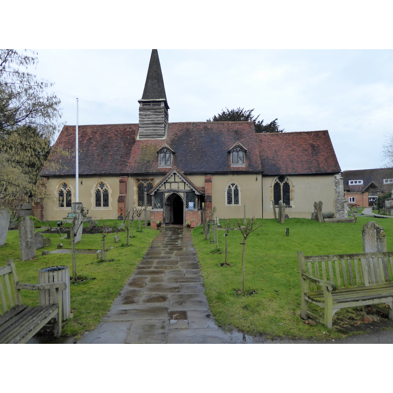 Source caption: "St Giles Church is in the heart of the old village of Ickenham and set back a little from the main road. It is a typical small aiseless church which is common in what was Middlesex. The bell turret has four bells. the earliest dating from 1510. Much of the church dates from the 14th and 15th centuries. It was enlarged early in the 16th century by a north aisle as wide and nearly as long as the rest of the church. Particularly interesting (according to Pevsner) are "the rustic timber-framed south porch and the pretty little timber bell-turret". The interior has a fine timber roof. The Jacobean wooden font is said to have been recovered from Swakelys where it was being used as a tea caddy or work table."