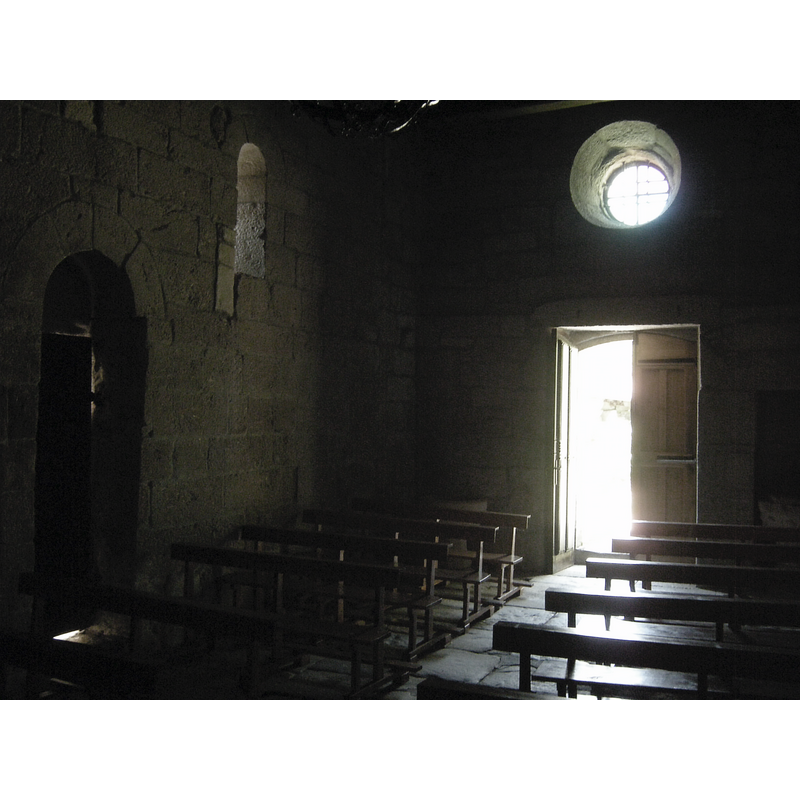Source caption: "Poco que destacar en su interior. El arco triunfal y la portada occidental fueron rehechos." -- Showing a partial view of a holy-water stoup to the left of the west entranceway and the baptismal font in the right corner alcove