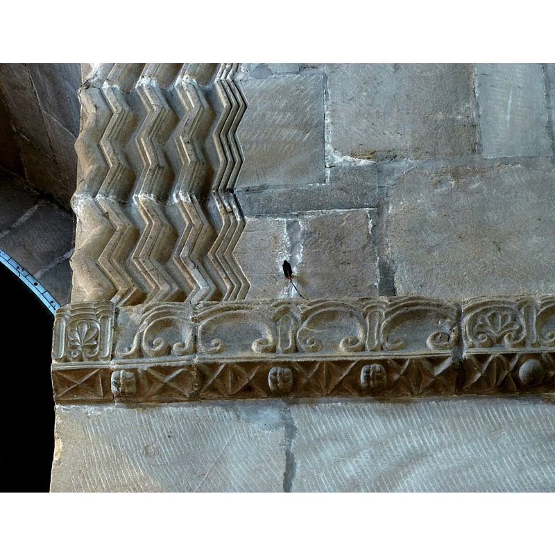 Source caption: "Detail of the west wall showing the zig-zag moulding of the west door surround and the decorative string course. The latter includes what appear to be precursors of ballflower ornamentation which did not develop until around a century later."