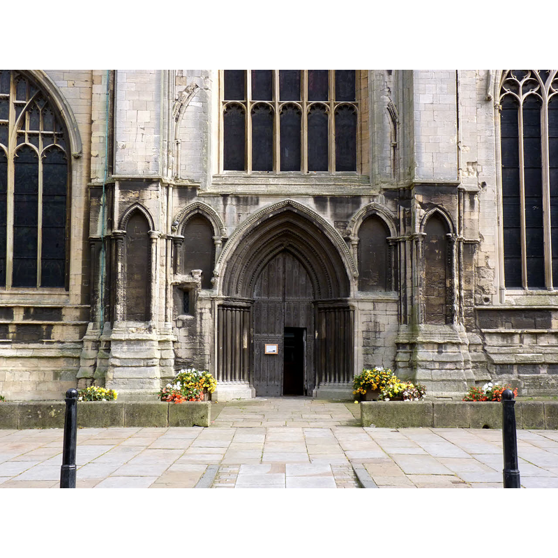Source caption: "West entrance, St Mary Magdalene Church. The doorway and adjoining arcading date from around 1220, contemporary with the tower. Similar arcading above has been cut through with the addition of a 5-light Perpendicular style window of the 15th century. The door itself is from the 14th century."