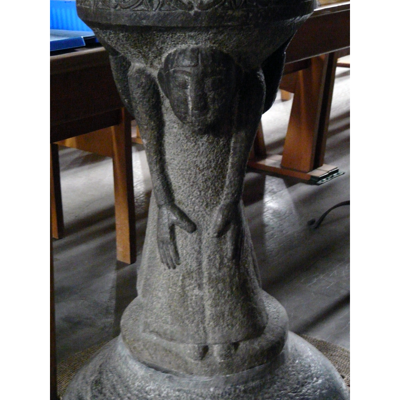 not clear whether male or female; unlike the atlante on the opposite side, this figure leans forward at the shoulders, on which the basin is supported; the armes extended down along the front, hands facing inwards with thumbs out; the long splaying robe (?) lets see only the tips of the feet