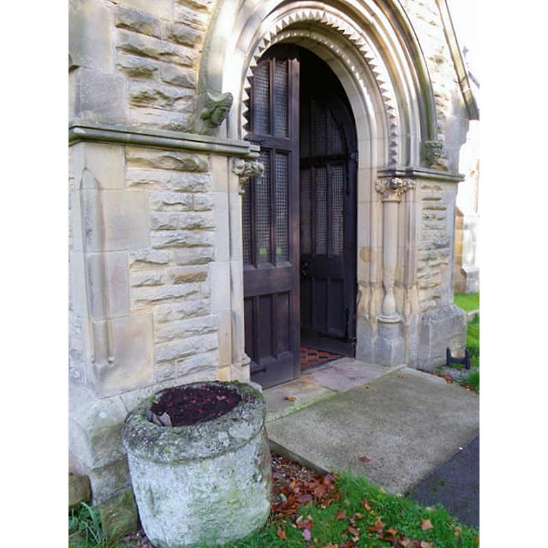 Source caption: "The south door [i.e. porch] of the church. The stone receptacle may have been a tub font in the original Norman church."
