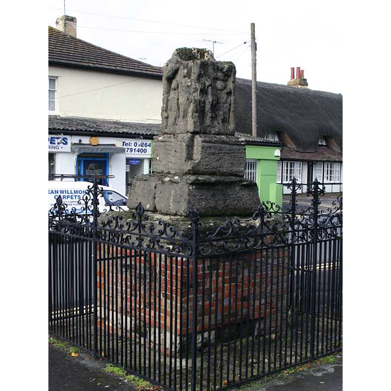 Listed in Historic England [Listing NGR: SU2645450925 ]: "Village cross and enclosing railings. c1300 and 1897. The Cross, Scheduled monument (List entry 1012691) of limestone, comprising two steps and base block carrying the lowest section of an elaborately carved cross shaft, much weathered, with scenes of the Ascension, the Descent from the Cross, the three Maries, and the briefing of the Apostles. The cross is set on a brick base and enclosed in wrought iron railings with frieze and crestings, ending in a crown on corner stanchions, and cross on each centre stanchion."