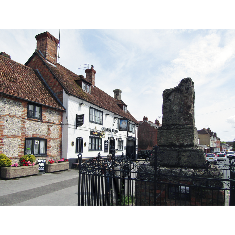 Listed in Historic England [Listing NGR: SU2645450925 ]: "Village cross and enclosing railings. c1300 and 1897. The Cross, Scheduled monument (List entry 1012691) of limestone, comprising two steps and base block carrying the lowest section of an elaborately carved cross shaft, much weathered, with scenes of the Ascension, the Descent from the Cross, the three Maries, and the briefing of the Apostles. The cross is set on a brick base and enclosed in wrought iron railings with frieze and crestings, ending in a crown on corner stanchions, and cross on each centre stanchion."