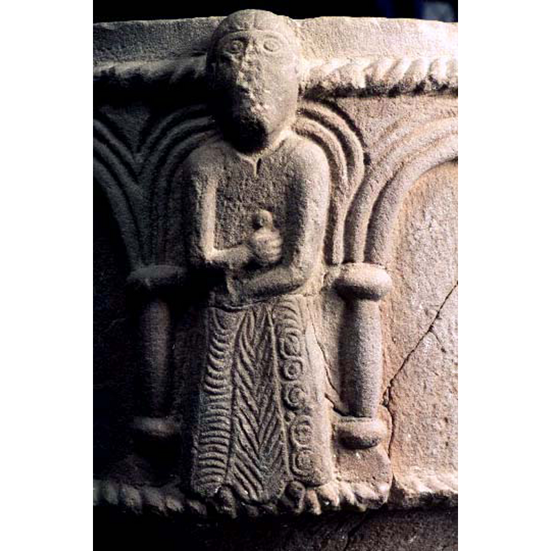 Source caption: "manlig gestalt" -- the figure stands facing the viewer, wearing a plain top but a richly decorated skirt that reaches down to his feet; the round hand, across his middle, holds something that looks like a sword or dagger handle, but the is no blade or scabbard visible
