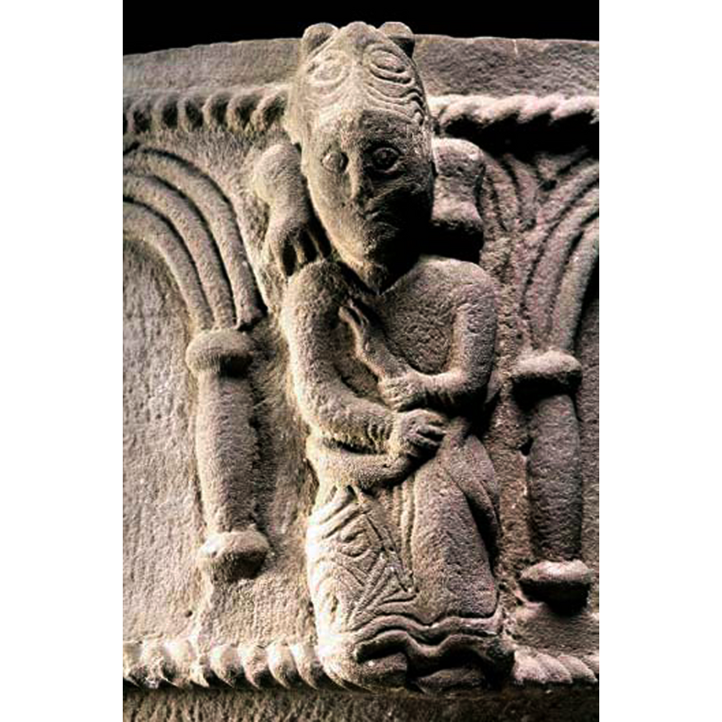 Seated human wearing animal hat and holding with both hands the body of a snake coiled around him.
