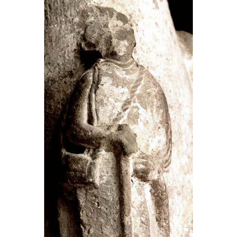 defaced figure wearing rectangular purse(?) on a long rope across the chest; is this a pilgrim, as suggested in the the SHM caption "hörnfigur i pilgrimsdräkt"?