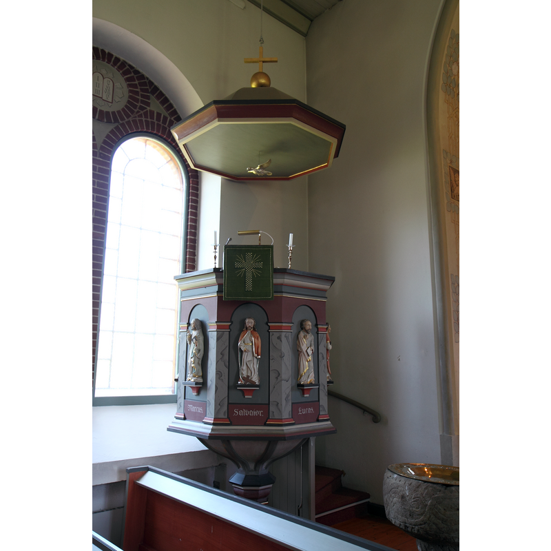 the medieval font is partially visible by the stairs leading up to the pulpit